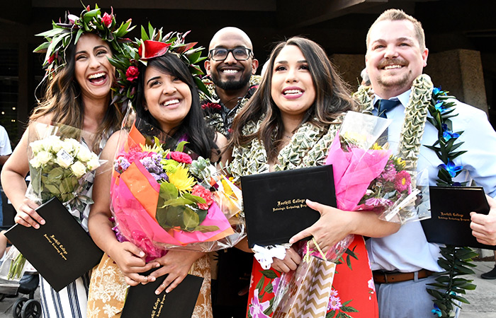 five graduates with holding flowers and degrees