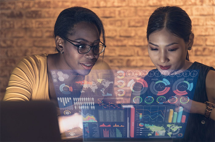 two young women of color look at data on a floating screen