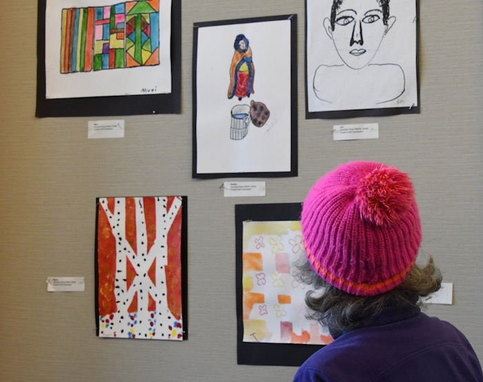 older woman with pink hat looking at artwork
