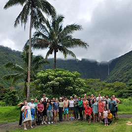 Large group of people under palm trees and lush green background
