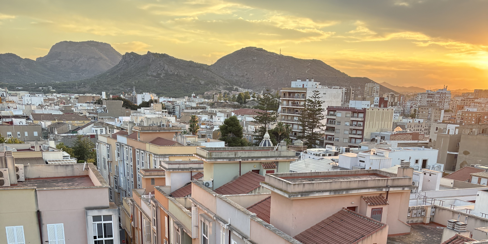 A vibrant city view surrounded by mountains and sunset