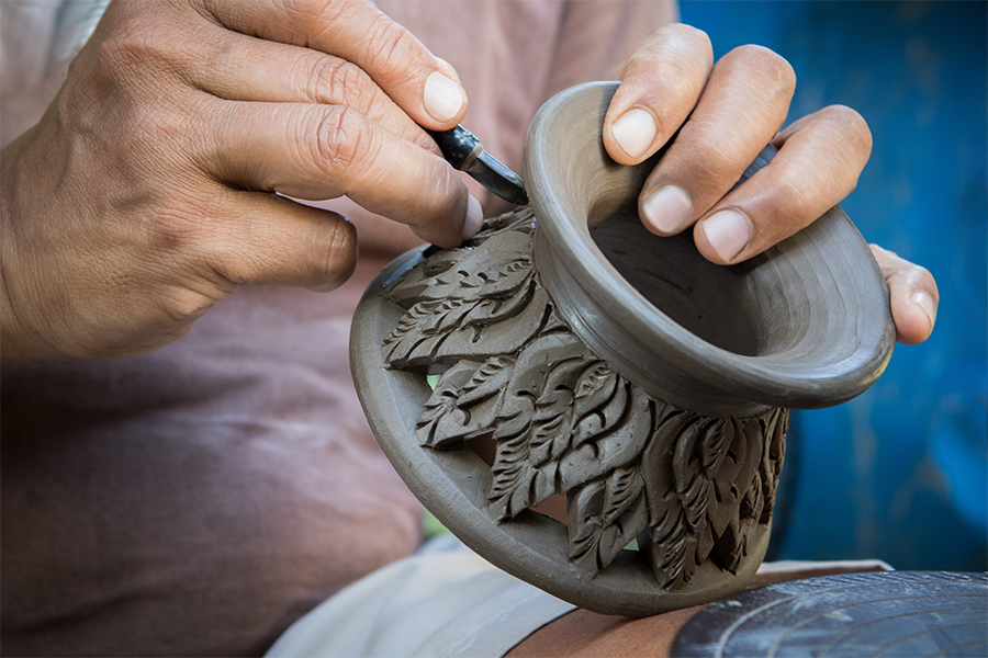Close-up of hands carving decorative details into a clay pottery piece