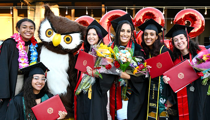 female grads in cap and gown with footsie mascot